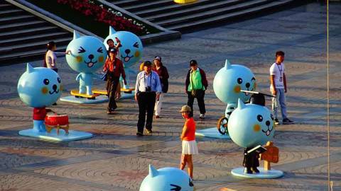 Crowd in China disinterested in large toy-cat installation.