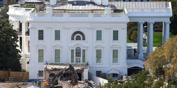 An excavator removes debris during demolition work at the White House East Wing site, where the former structure—associated with the planned White House ballroom—has been torn down, leaving piles of rubble and exposed foundations within the grounds of the U.S. presidential residence.