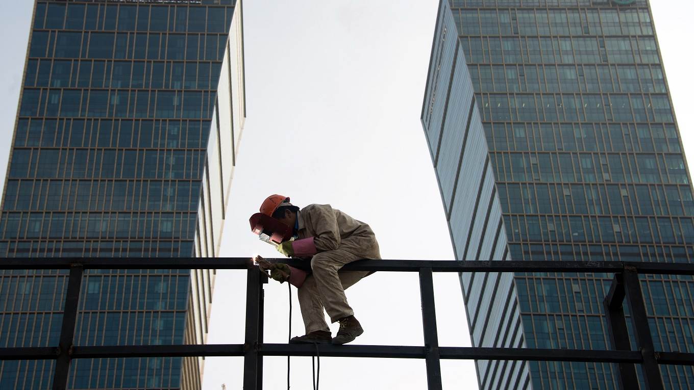 A worker welds a scaffolding in front of the headquarters of the Agricultural Bank of China