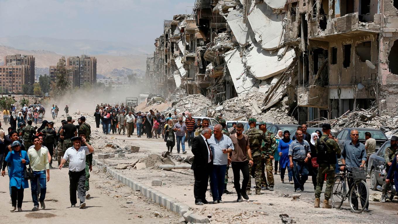Civilians and pro-government forces walk down the destroyed Thalateen Street in the Yarmuk