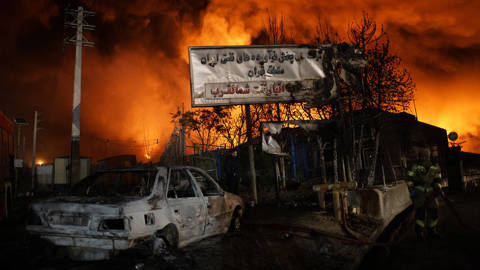 Fire and thick smoke erupting from the Shahran oil depot in Tehran, Iran, on March 8, 2026, after US and Israeli attacks, with damaged fuel tankers and vehicles visible in the foreground.