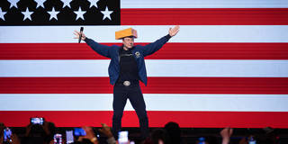 Elon Musk con un sombrero de queso frente a la bandera de Estados Unidos.
