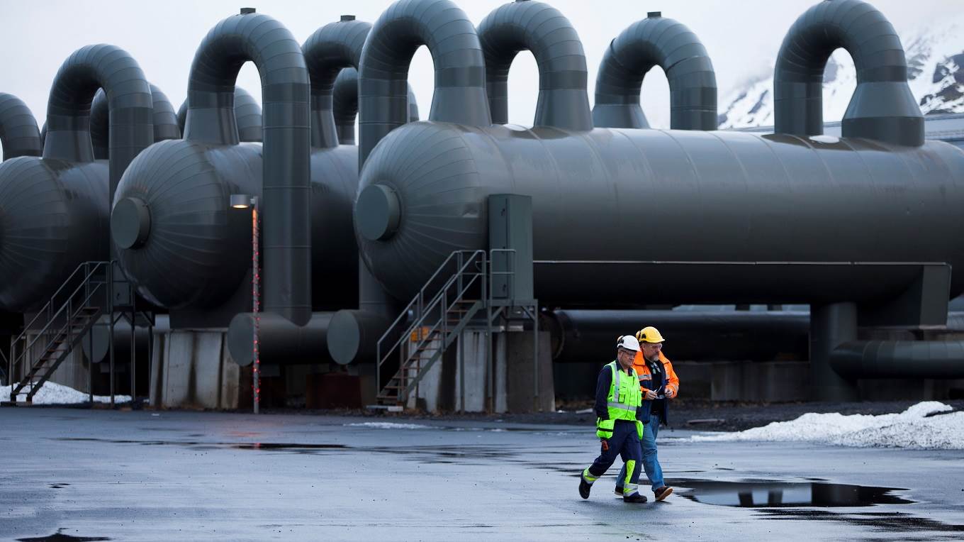 Workers walk past steam storage tanks at Reykjavik Energy's Hellisheidi Geothermal Power Plant
