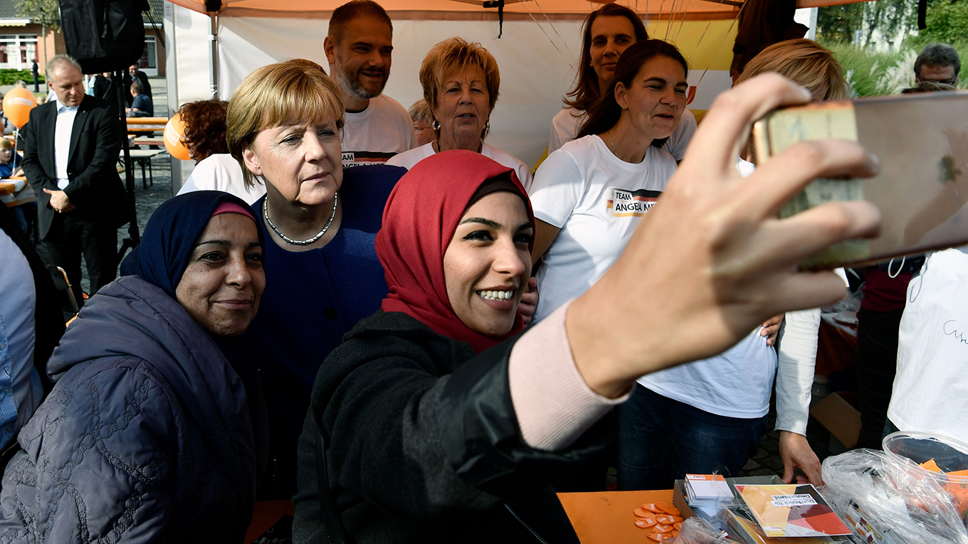 A syrian refugee poses for a selfie photo with Angela Merkel