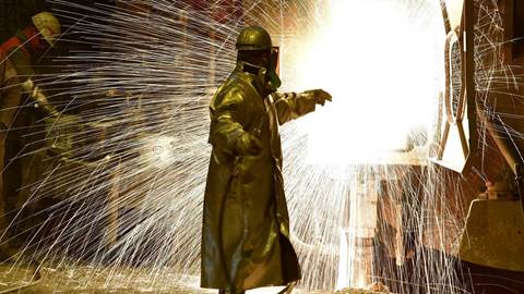  An employee works in front of the blast furnace past rolls of sheet steel at a mill of German steel producer Salzgitter AG 
