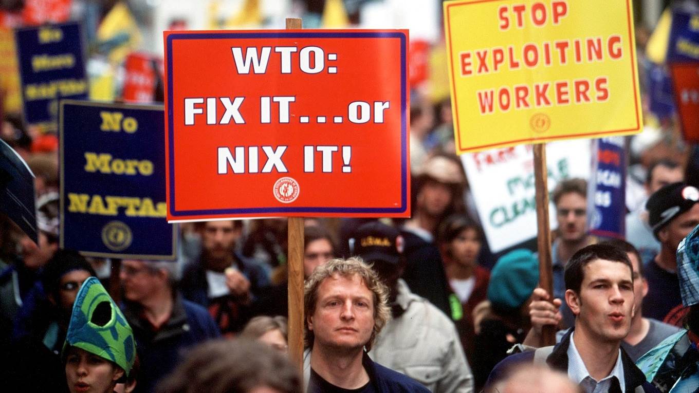 Protesters hold signs while standing a few blocks away from the World Trade Organization