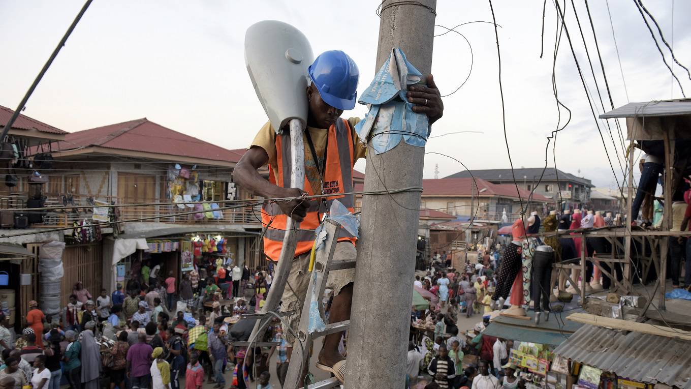 A volunteer sets up a street lamp in the market area of the Oshodi district in Lagos