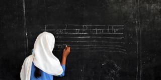 A Pakistani female student writes a sentence on a black board