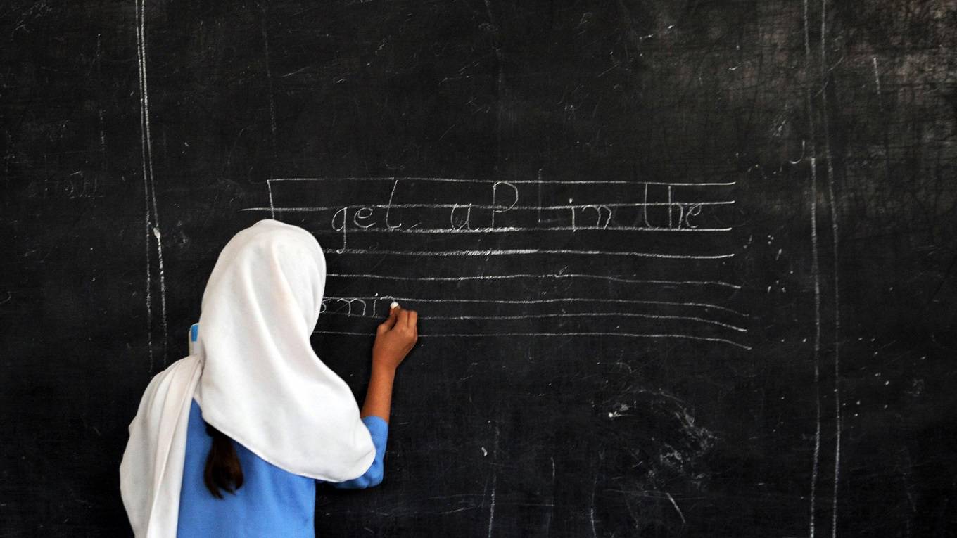 A Pakistani female student writes a sentence on a black board