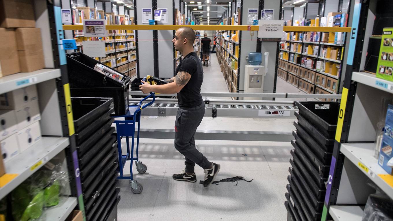 A worker pushes a trolley as he walks between goods stored inside an Amazon.co.uk fulfillment centre