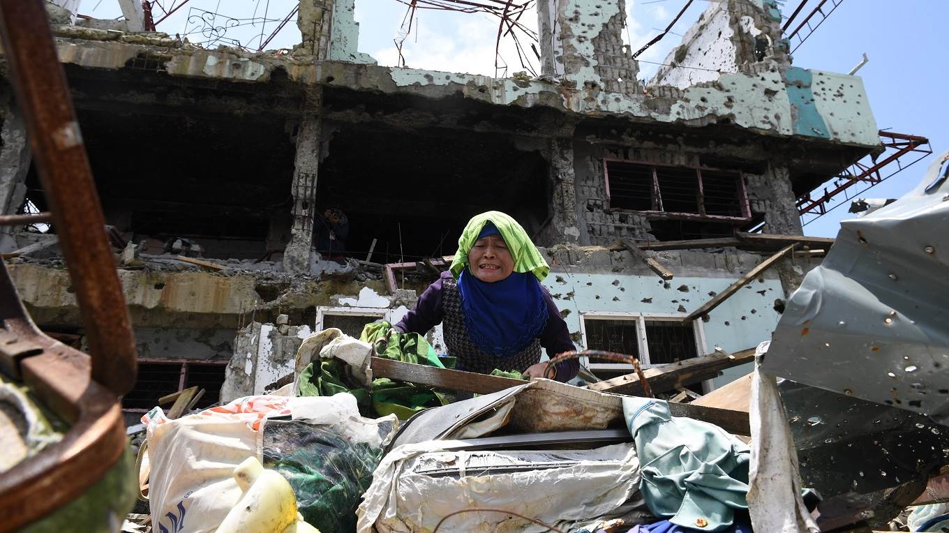 A resident tries to collect salvageable belongings from her destroyed house during a visit to the main battle area in Marawi City