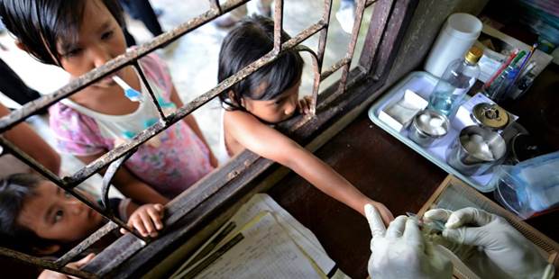 A Thai health official performs a blood test on children at a Malaria clinic 