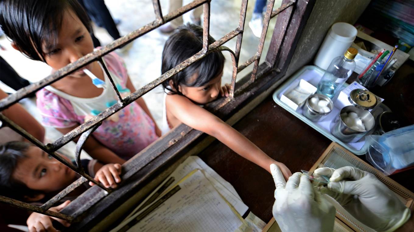 A Thai health official performs a blood test on children at a Malaria clinic