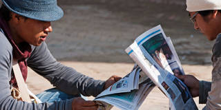 Two teenage Nepali males reading newspapers