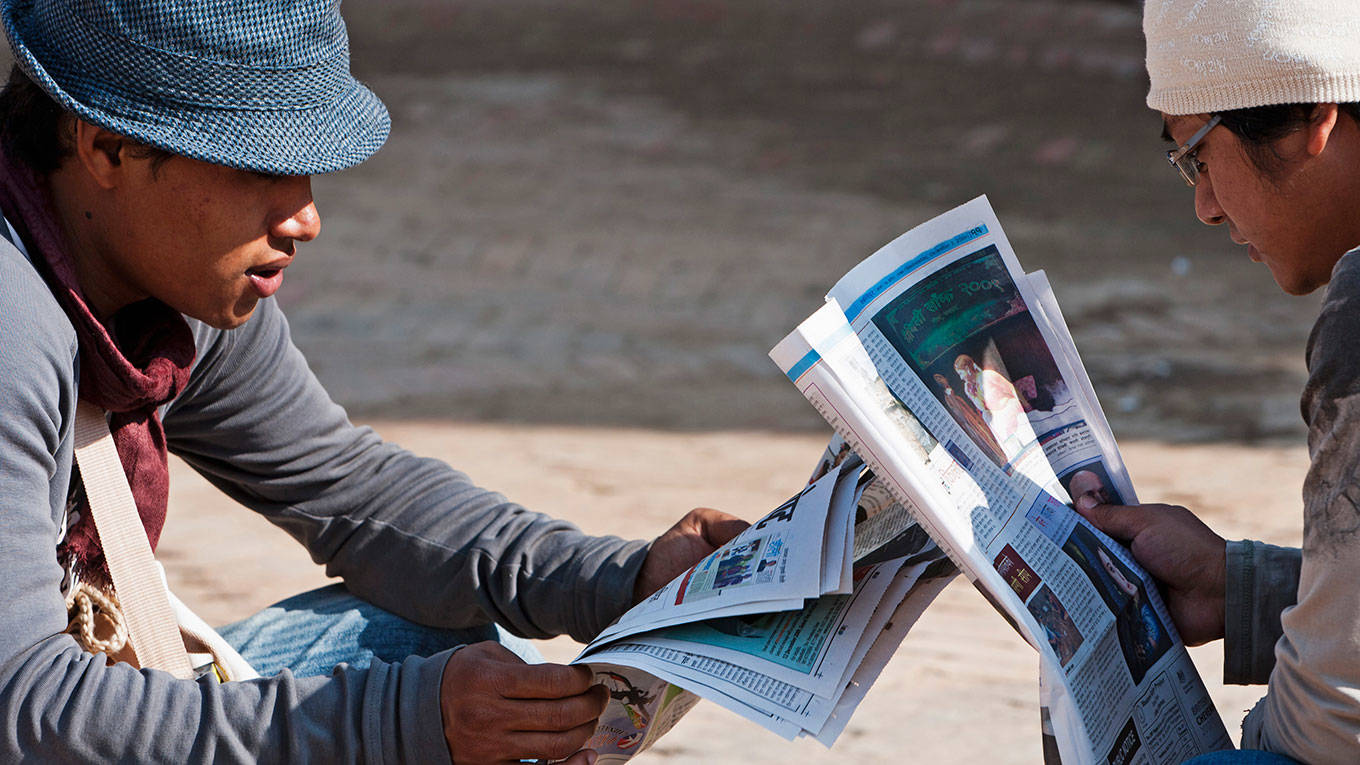 Two teenage Nepali males reading newspapers