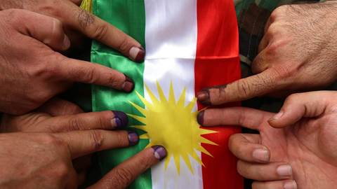 Ink-stained fingers in front of a Kurdish flag 