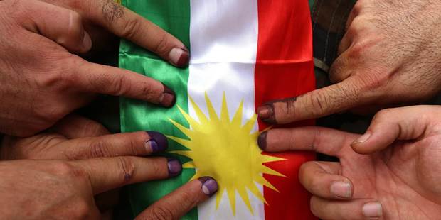 Ink-stained fingers in front of a Kurdish flag 