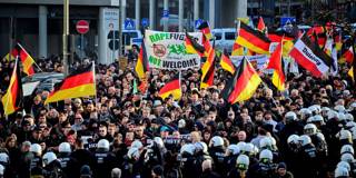 Protesters wave German flags, alongside a banner saying 'Rapefugees Not Welcome'