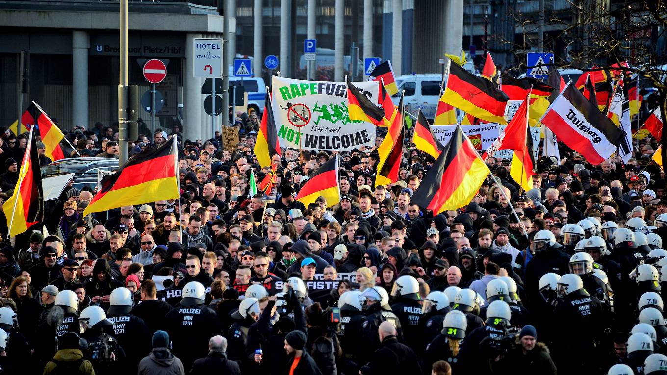 Protesters wave German flags, alongside a banner saying 'Rapefugees Not Welcome'