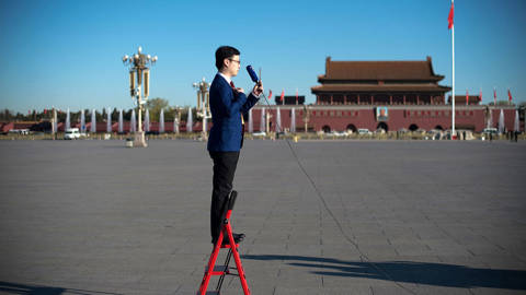  A television journalist stands on a ladder