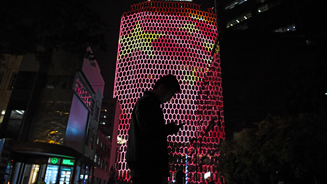 A man looks at his phone near a giant image of the Chinese national flag 