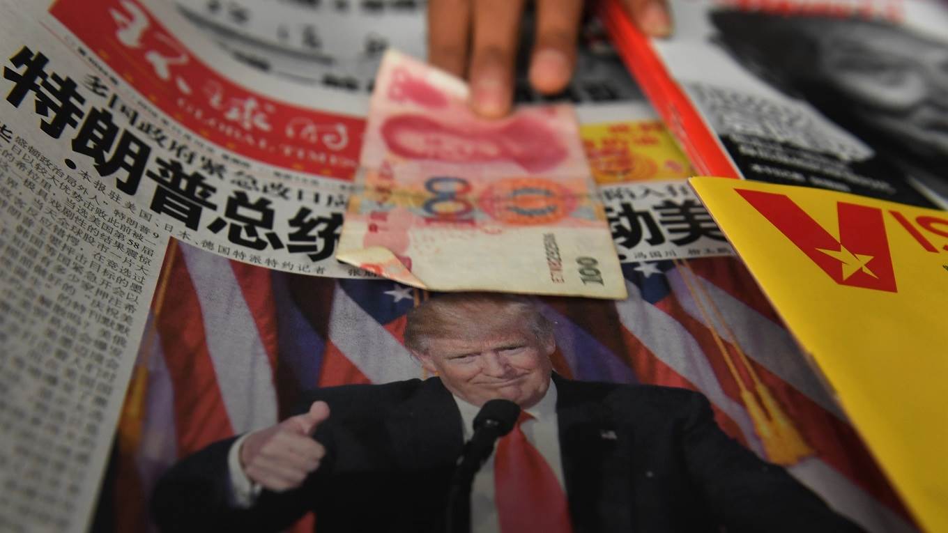 A vendor picks up a 100 yuan note above a newspaper featuring a photo of US president Donald Trump