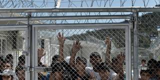 Young migrants and refugees stand at a fence of the Moria detention center
