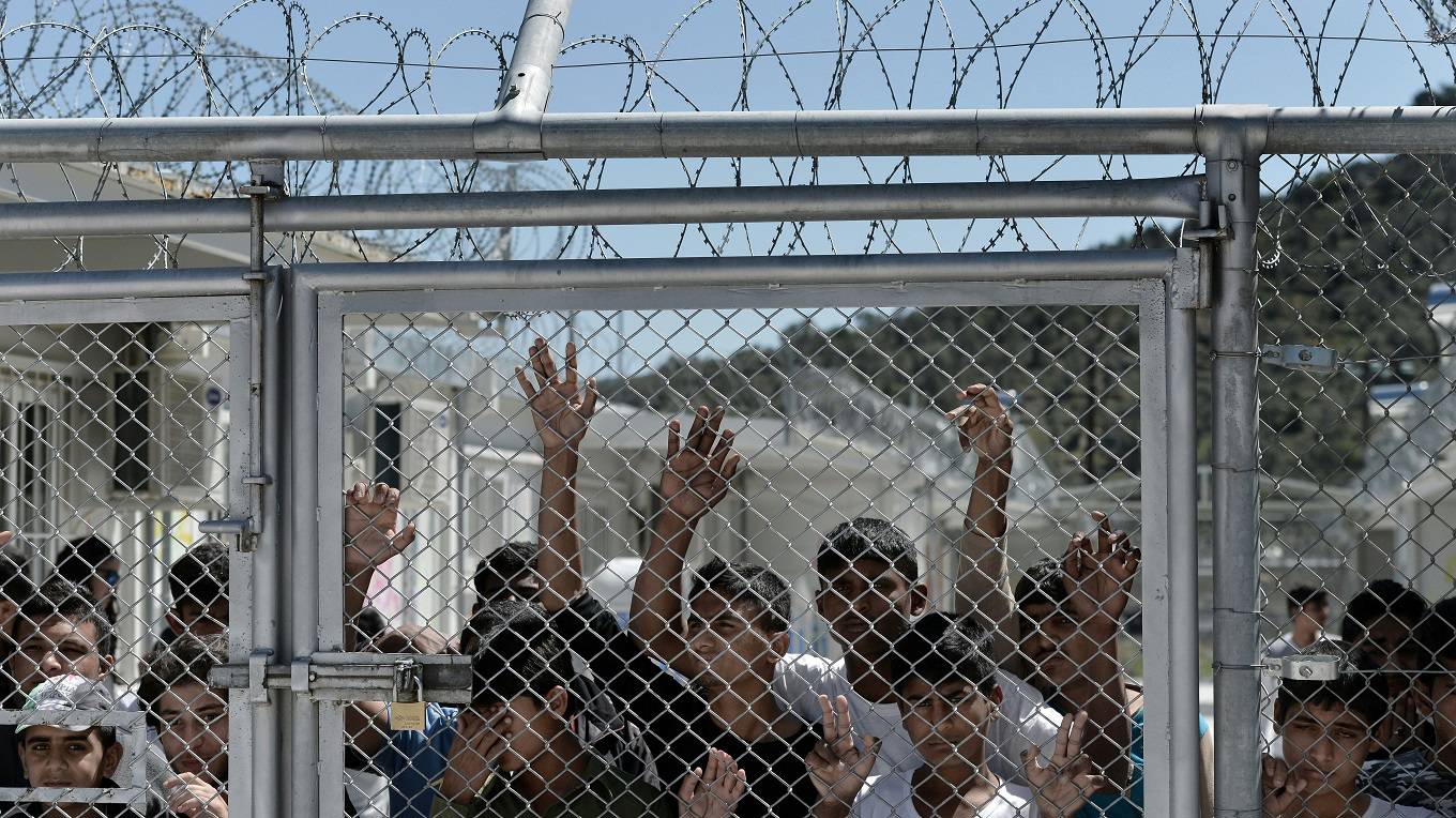 Young migrants and refugees stand at a fence of the Moria detention center