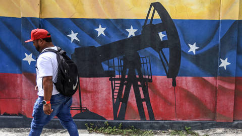 Man walks by a mural of an oil pump on the Venezuelan flag.