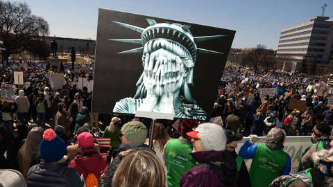 Protestor holds sign of edited Statue of Liberty with hands over face crying.