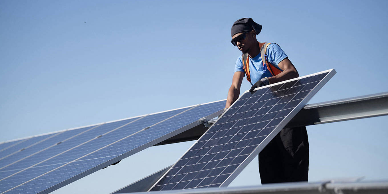 South African worker installing a solar panel in a new plant