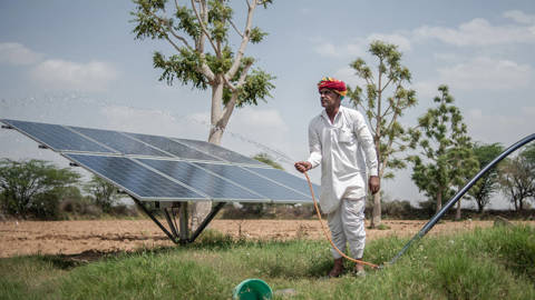 Indian farmer waters his yard with solar panels nearby