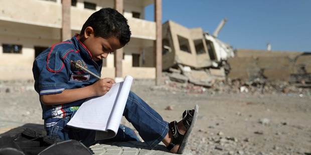 A Yemeni boy school writes as he sits outside a school 