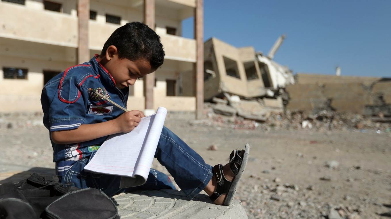 A Yemeni boy school writes as he sits outside a school
