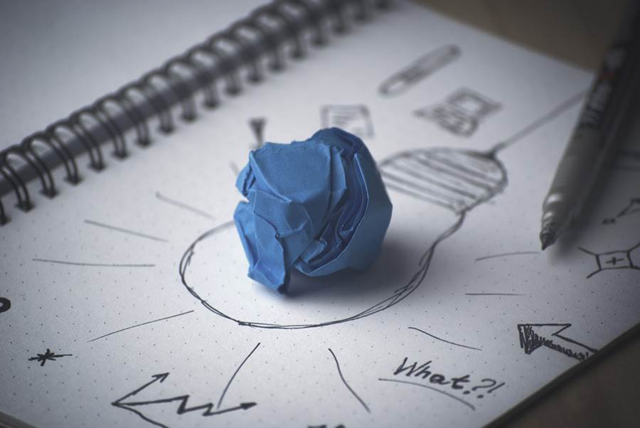 Crumpled paper on notebook with drawn image of light bulb.