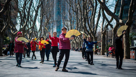 Women dance with fans in a park on a sunny day in Shanghai