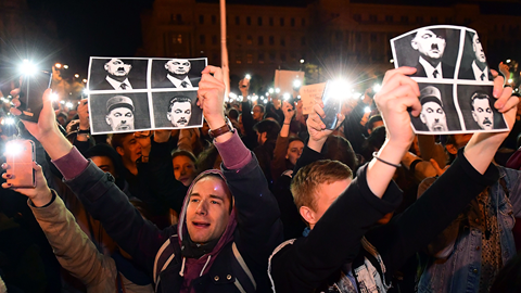 A student shows a combo pictures of three dictators, Austrian born Hitler, Castro and Stalin with Viktor Orban