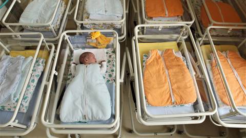 A 4-day-old newborn baby, who has been placed among empty baby beds 