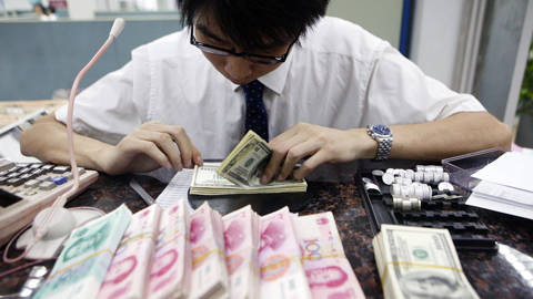 A clerk counting stacks of Chinese yuan and US dollars