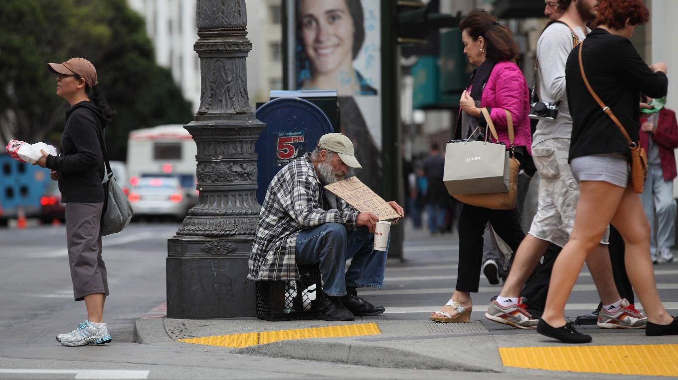 A homeless man holds a sign as he panhandles for spare change