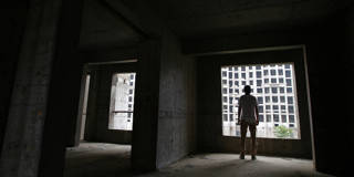 A man looks out from an unfinished apartment building in China.