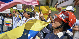 Relatives of Venezuelan political prisoners protesting outside the United Nations headquarters in Caracas, holding signs and banners on February 18, 2026, as they demand the approval of an amnesty law and the release of detainees following repeated postponements of the legislation. The demonstrators look concerned and determined in a crowded street scene.