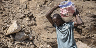 A miner in Gidan Kwano, Nasarawa State, Nigeria, carries a heavy sack of lithium-bearing stones over his shoulders at a mining site, illustrating the labor-intensive extraction driving global demand for critical minerals used in clean energy technologies.