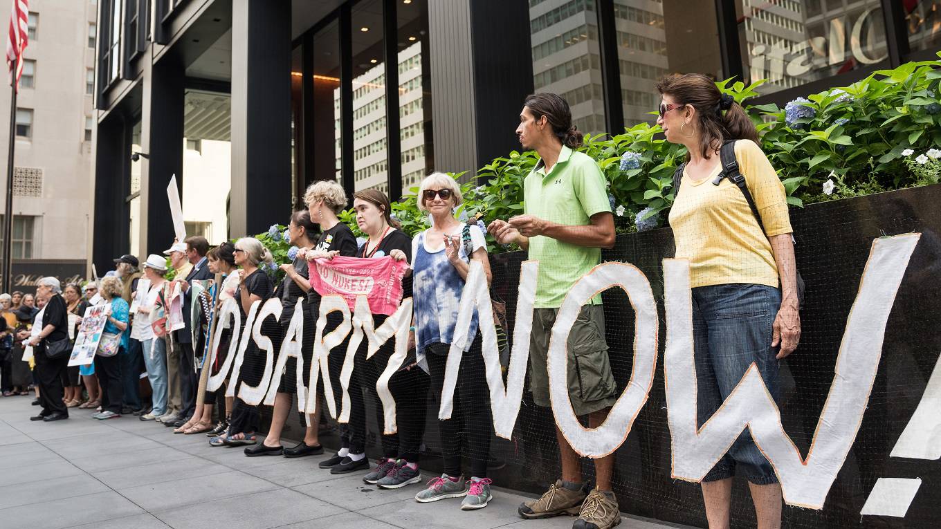 Peace activists hold banners and signs while standing on the sidewalk in front of the Consulate General of Japan in New York