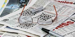 Glasses on newspaper featuring markets and crossword.
