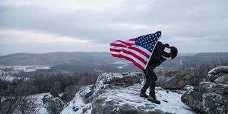 Man holding an American flag in snowy mountains.
